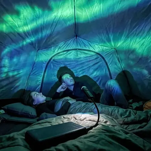 Aurora verde e blu proiettata sul telo di una tenda di notte